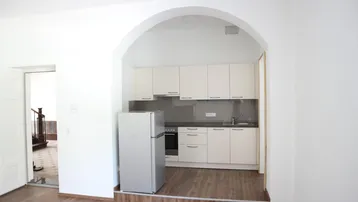 Kleine Einbauküche in einem hellen Raum mit Holzboden und offenem Durchgang.