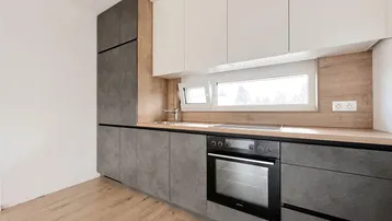 Moderne Küche mit grauen Unterschränken, weißen Oberschränken, Holzarbeitsplatte und Fenster.