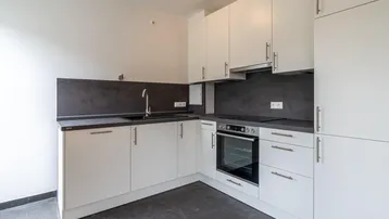 Moderne Einbauküche mit weißen Schränken, dunkler Arbeitsplatte und integriertem Backofen.