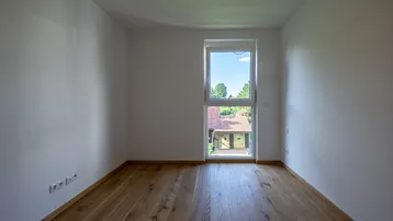 Helles Schlafzimmer mit Holzboden und einem Fenster mit Blick ins Grüne.
