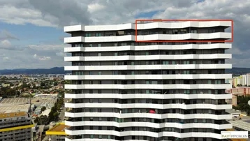 Nahaufnahme der modernen Fassade eines Hochhauses mit zahlreichen Balkonen und einer städtischen Umgebung.