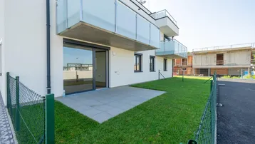 Moderne Wohnanlage mit privater Terrasse und Rasenfläche, umgeben von einem Zaun.