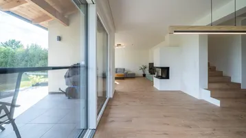 Helles, offenes Wohnzimmer mit Kamin, Holzboden und Zugang zur überdachten Terrasse.