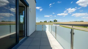 Geräumiger Balkon mit Glasbrüstung und weitem Blick über die umliegende Landschaft.