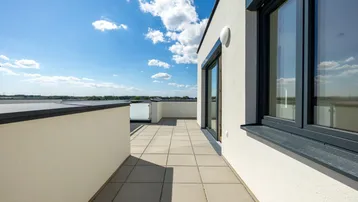 Geräumige Dachterrasse mit Fliesenboden und weitem Blick unter blauem Himmel.