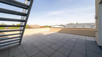 Geräumige Dachterrasse mit Fliesenboden und Metalltreppe, bietet Platz für Entspannung im Freien.