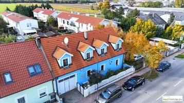 Luftaufnahme eines blauen Reihenhauses mit roten Dachziegeln und Gauben in einer Wohnsiedlung.