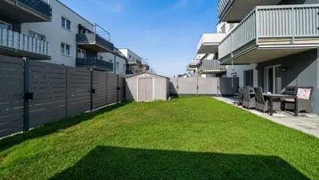 Gepflegter Gartenbereich mit Rasenfläche, Gartenhaus und angrenzender Terrasse zwischen Wohngebäuden.