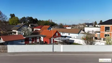 Überblick über eine Wohnsiedlung mit verschiedenen Häusern und einer Straße unter blauem Himmel.