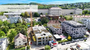 Luftaufnahme einer Baustelle im Mai 2026, umgeben von Wohngebäuden und grünen Hügeln.