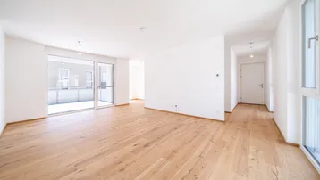 Helles, leeres Zimmer mit Holzboden und Zugang zu einem Balkon, ideal für einen Wohnbereich.