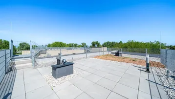 Geräumige Dachterrasse mit Fliesenboden und Kiesbereichen unter blauem Himmel.