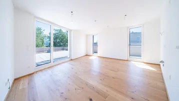Helles, leeres Zimmer mit Holzboden und großen Fenstern, die Zugang zu einer Terrasse bieten.