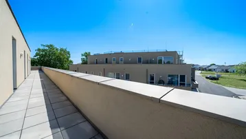 Blick von der Dachterrasse entlang der Gebäudefassade auf die umliegende Bebauung und Straße.