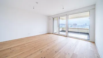 Helles, leeres Zimmer mit Holzboden und Zugang zu einem großen Balkon.