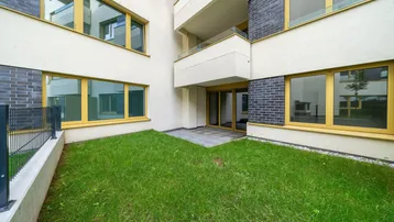 Außenansicht eines modernen Gebäudes mit kleinem Rasenbereich und Zugang zur Terrasse.