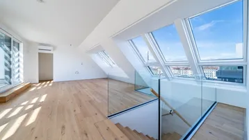 Helles, offenes Dachgeschoss mit Holzboden, großen Fenstern und Blick auf die Stadt.