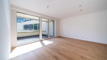 Helles Zimmer mit Holzboden und Zugang zu einem Balkon, ideal als Wohn- oder Schlafbereich.