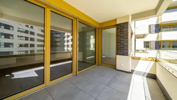 Heller Balkon mit Fliesenboden und Glasgeländer, bietet einen sonnigen Außenbereich mit Blick auf umliegende Gebäude.