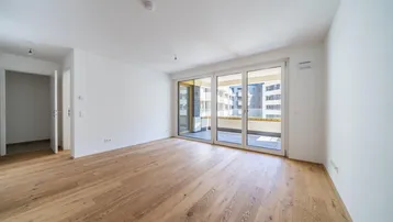 Helles, leeres Wohnzimmer mit neuem Parkettboden und Zugang zu einem Balkon.