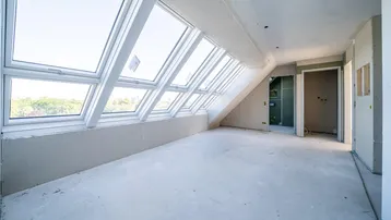 Unfertiger Dachgeschossraum mit vielen Dachfenstern und Blick ins Grüne, bereit für den Ausbau.