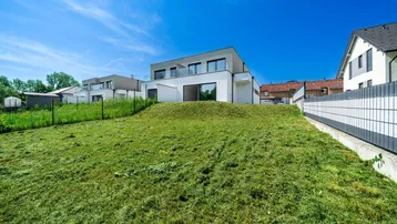 Moderne Architektur des Neubaus mit großen Fensterfronten und Balkonen, eingebettet in die grüne Umgebung.