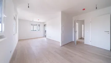 Helles, leeres Wohnzimmer mit hellem Parkettboden und weißen Wänden, bereit zur Einrichtung.