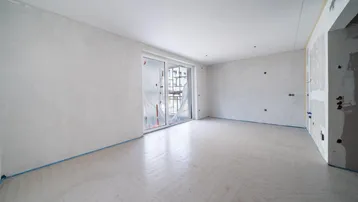 Unfertiger Innenraum mit Rohbauwänden und Zugang zu einem Balkon oder einer Terrasse durch große Fenster.