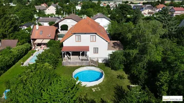 Luftaufnahme eines Einfamilienhauses mit Garten, Terrasse und oberirdischem Pool in grüner Umgebung.