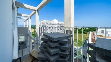 Unfertiger Balkon mit Baumaterialien und Blick auf die umliegenden Gebäude und Grünflächen.
