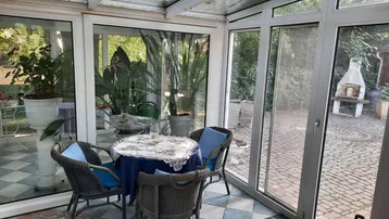 Heller Wintergarten mit Essbereich und Blick in den Garten mit Grillplatz.