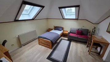 Gemütliches Schlafzimmer im Dachgeschoss mit Einzelbett, Sofa, Schreibtisch und zwei Dachfenstern.