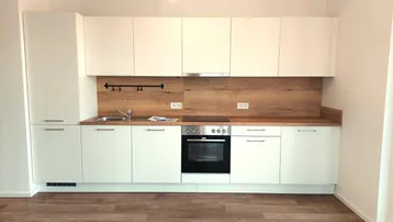 Moderne Einbauküche mit weißen Hochglanzfronten, Holzoptik-Arbeitsplatte und integrierten Geräten.