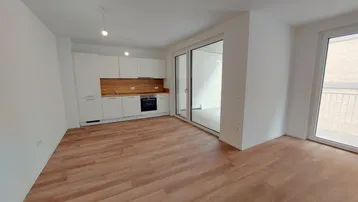 Heller, offener Wohnbereich mit integrierter Küche, Laminatboden und Zugang zu einem Balkon.