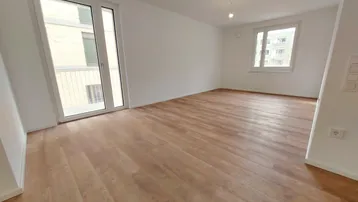 Helles Wohnzimmer mit Laminatboden, großen Fenstern und Zugang zu einem französischen Balkon.