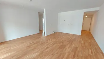 Heller, leerer Wohnbereich mit neuem Parkettboden und weißen Wänden in einem Neubau.