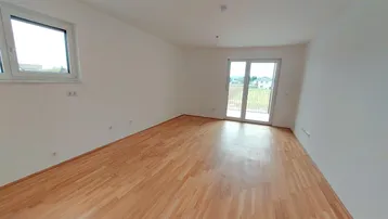 Helles, leeres Zimmer mit Parkettboden und Zugang zu einem Balkon, ideal als Wohnbereich.