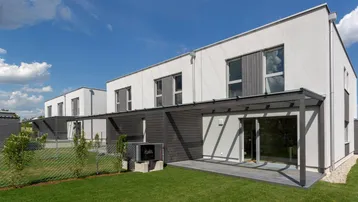 Moderne Reihenhäuser mit privatem Garten und überdachter Terrasse unter blauem Himmel.