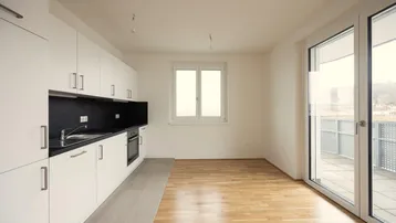 Moderne Küche mit weißen Schränken, schwarzer Arbeitsplatte und Zugang zu einem Balkon.