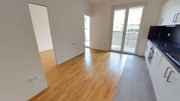 Heller offener Wohnbereich mit integrierter Küche, Parkettboden und Zugang zu einem Balkon.