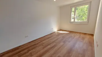 Helles Schlafzimmer mit Laminatboden und großem Fenster mit Blick ins Grüne.
