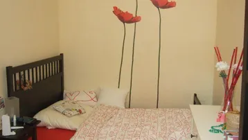 Helles Schlafzimmer mit Einzelbett, Schreibtisch und dekorativen Mohnblumen an der Wand.