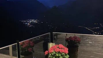 Terrasse bei Nacht mit beleuchteten Blumenkübeln und einem weiten Blick auf das beleuchtete Tal.