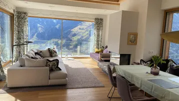 Großzügiger Wohn- und Essbereich mit Holzbalken, Kamin und Panoramablick auf die Bergwelt.