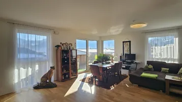 Helles Wohn- und Esszimmer mit Holzboden, großen Fenstern und Zugang zum Außenbereich.