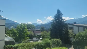 Panoramablick auf die umliegende Berglandschaft und grüne Umgebung an einem sonnigen Tag.