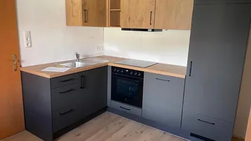 Moderne L-förmige Küche mit dunklen Unterschränken, Holz-Oberschränken und integrierten Geräten.