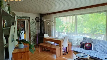 Heller Wohn-Essbereich mit Holztisch, Sitzbänken und Kaminofen mit Blick ins Grüne.