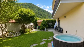 Geräumiger Gartenbereich mit Whirlpool, Grillplatz und Blick auf die umliegenden Berge.