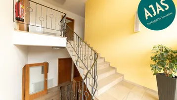 Geräumiges Treppenhaus mit gelber Wand, Steinfliesenboden und schmiedeeisernem Geländer.